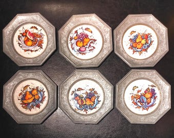 Puede incluir: Seis platos decorativos octogonales con un marco de metal color peltre. Cada plato presenta un diseño central de frutas coloridas, incluyendo uvas, melocotones y peras, sobre un fondo blanco. Los platos están dispuestos en una cuadrícula de 2x3.
