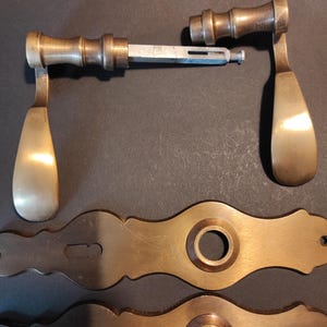 May include: Antique brass door hardware set, including two handles and two decorative backplates. The handles have a classic teardrop design and are connected by a metal rod. The backplates feature a circular center and decorative edges.