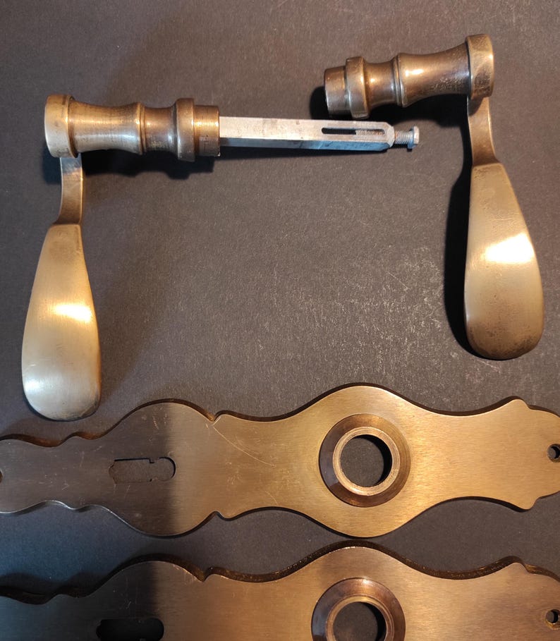 May include: Antique brass door hardware set, including two handles and two decorative backplates. The handles have a classic teardrop design and are connected by a metal rod. The backplates feature a circular center and decorative edges.