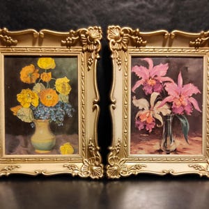 Puede incluir: Dos pinturas florales enmarcadas. Una presenta flores amarillas y naranjas en un jarrón amarillo, la otra muestra orquídeas rosas y blancas en un jarrón de cristal. Ambas pinturas están en marcos dorados ornamentados.