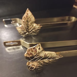 Può includere: Due fermatende in metallo color oro. Ogni fermatenda presenta un design a foglia all'estremità. Le foglie hanno venature dettagliate. I fermatenda sono progettati per tenere le tende aperte.