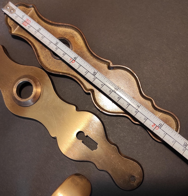 May include: Close-up of antique brass door hardware, including a keyhole plate and a decorative backplate. A measuring tape shows the backplate is approximately 8 inches long. The hardware has a warm, aged patina.