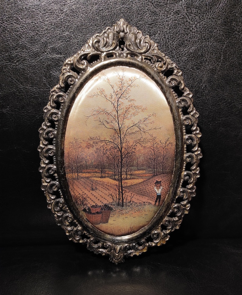 May include: An oval-shaped framed print of a painting depicting a rural landscape with a lone figure in the foreground. The frame is ornate and silver in color.