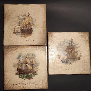 May include: Four square ceramic tiles with nautical scenes. Each tile features a detailed illustration of a sailing ship on the sea, with text at the bottom. The tiles have a distressed, aged appearance with brown edges.