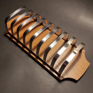 Pode incluir: Um suporte de pão de madeira com um design de arame cromado. O suporte tem um acabamento de madeira natural e é projetado para conter vários pães.