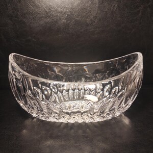 May include: A clear, oval-shaped glass bowl with a textured, cut-glass design. The bowl has a wide opening and a curved shape, suitable for serving or display. The intricate pattern catches the light, creating a sparkling effect.