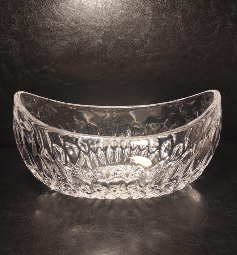 May include: A clear, oval-shaped glass bowl with a textured, cut-glass design. The bowl has a wide opening and a curved shape, suitable for serving or display. The intricate pattern catches the light, creating a sparkling effect.