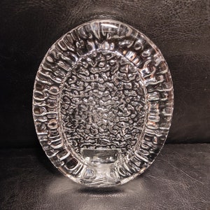 May include: A clear glass oval dish with a textured surface. The dish has a raised rim and a smooth, flat bottom.