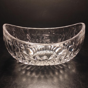 May include: Clear glass serving bowl with a curved, boat-like shape. The bowl features a detailed, textured pattern around the exterior. The bowl is designed to be used for serving food.