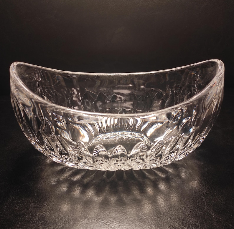 May include: Clear glass serving bowl with a curved, boat-like shape. The bowl features a detailed, textured pattern around the exterior. The bowl is designed to be used for serving food.