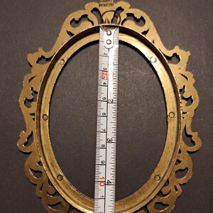 Puede incluir: Marco de fotos ovalado de lat&oacute;n con adornos decorativos. La altura interior del marco es de aproximadamente 10 cm, como se muestra en una cinta m&eacute;trica. El marco est&aacute; marcado "MADE IN ITALY".