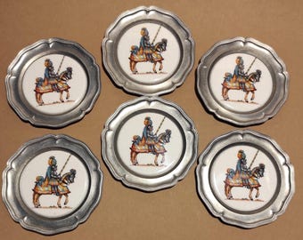 Puede incluir: Juego de seis platos decorativos con borde festoneado. Cada plato presenta una imagen central de una persona a caballo con atuendo colorido. Los platos tienen un borde de metal plateado y un centro blanco.