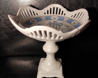 May include: White porcelain pedestal bowl with a blue and white floral design. The bowl has a scalloped edge and a delicate openwork pattern.