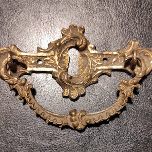 May include: Ornate gold-toned metal door handle with a keyhole and a decorative ring pull.