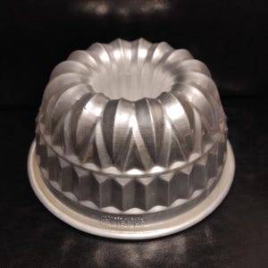 Könnte beinhalten: Eine silberfarbene Metall-Bundtkuchenform mit geriffeltem Design. Die Form hat einen herausnehmbaren Boden und ein Etikett mit der Aufschrift "Made in USA  Wilton Art".