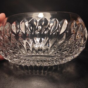 May include: A clear, cut-glass bowl with a detailed, repeating leaf-like pattern. The bowl has a rounded shape and a textured exterior, reflecting light. The design is symmetrical, creating a decorative and elegant appearance. The bowl is likely used for serving or display.