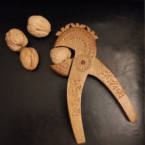 Op de afbeelding: Een houten notenkraker met ingewikkelde houtsnijwerk in de vorm van een vogel. De notenkraker is open, met een walnoot erin. Er liggen drie walnoten op de tafel.