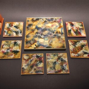 Puede incluir: Conjunto de seis posavasos coloridos con un diseño de mármol. Los posavasos están hechos de resina y tienen un acabado brillante. Los posavasos son de forma cuadrada y miden aproximadamente 10 cm de lado. Los posavasos están en un soporte con una base de madera.