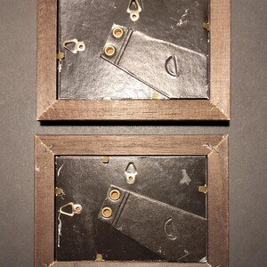 May include: Two brown wooden picture frames with black cardboard backing and gold-coloured hanging hardware. The frames are empty.