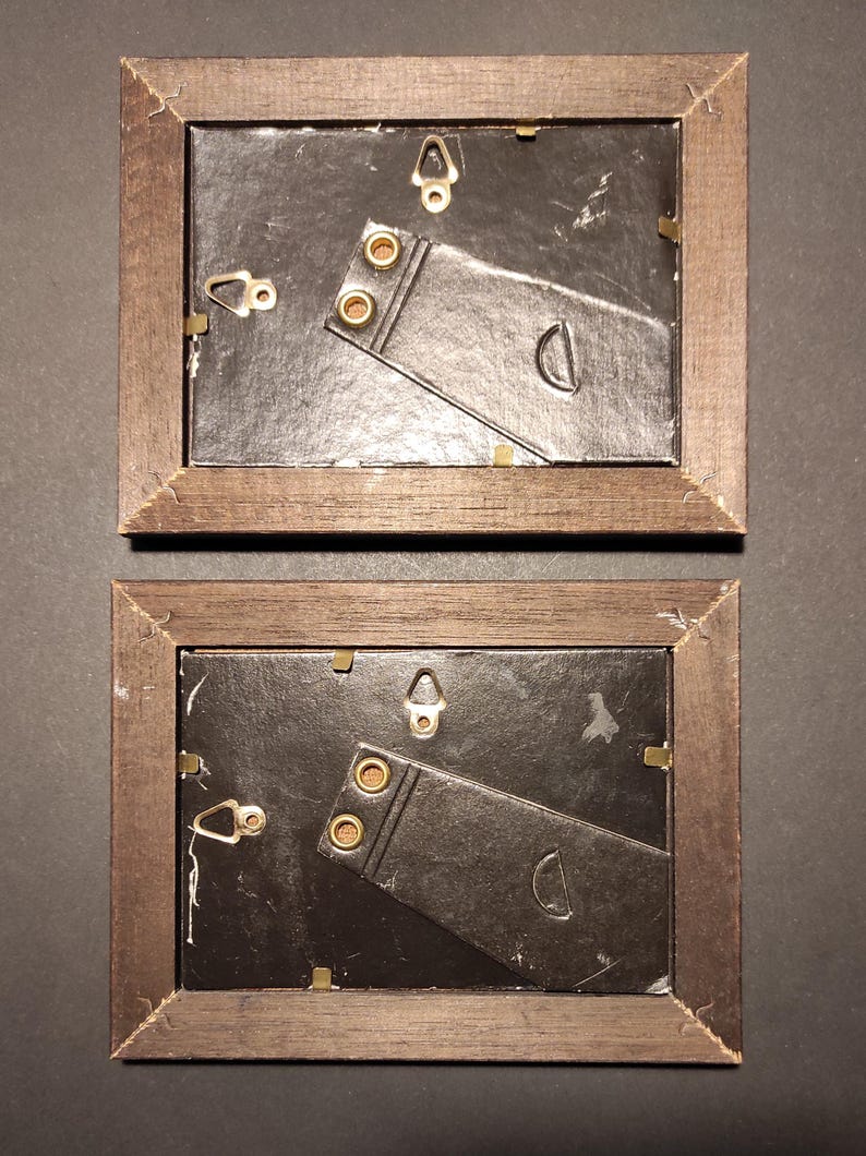 May include: Two brown wooden picture frames with black cardboard backing and gold-coloured hanging hardware. The frames are empty.