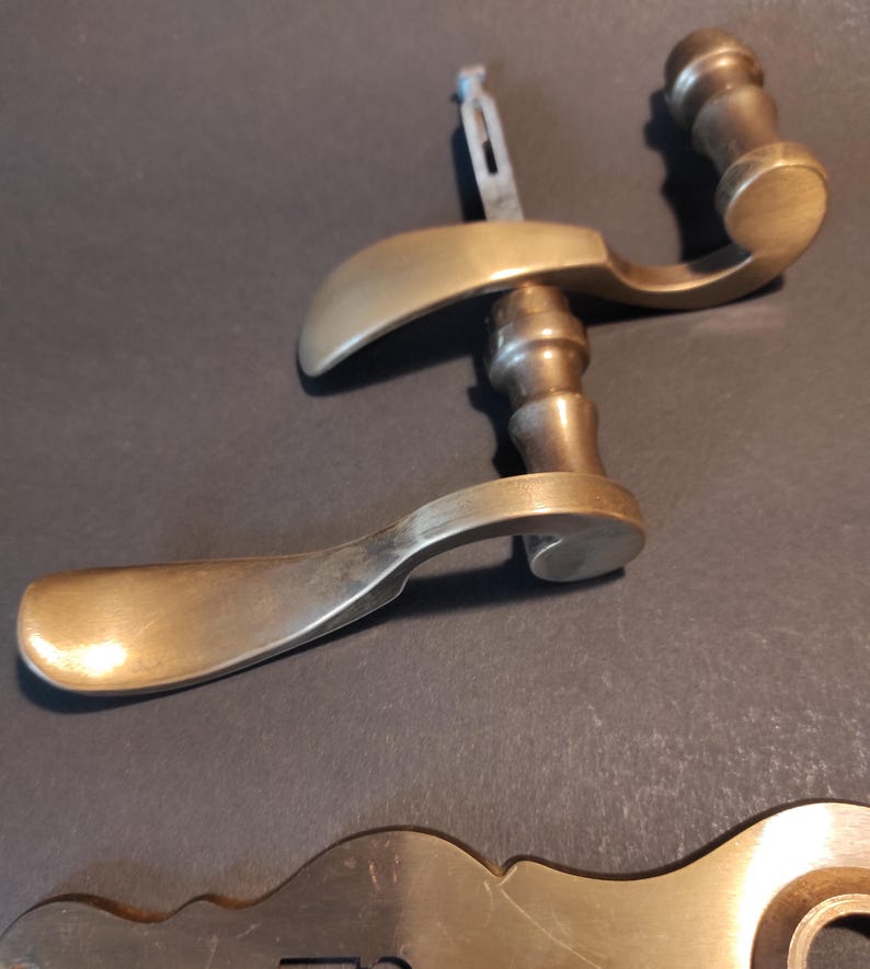 May include: Two antique brass door handles with a curved design. The handles have a warm, golden hue and a classic, vintage aesthetic. The image also shows a brass keyhole plate.