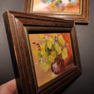 May include: A framed painting of yellow flowers in a purple vase. The painting is set against a warm orange background.