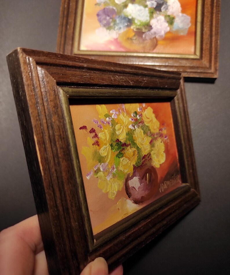 May include: A framed painting of yellow flowers in a purple vase. The painting is set against a warm orange background.