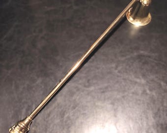 Könnte beinhalten: Ein goldfarbener Kerzenlöscher mit einem langen, schlanken Griff und einer glockenförmigen Tasse. Der Griff hat ein dekoratives, verziertes Ende. Dieses Zubehör ist für das sichere und saubere Löschen von Kerzen konzipiert.