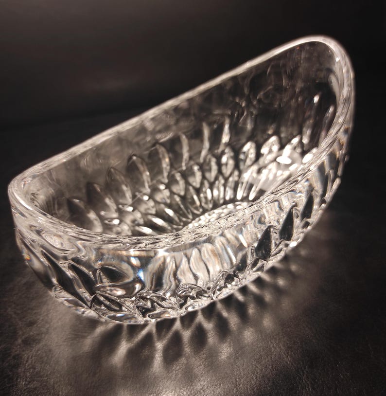 May include: A clear, oval-shaped glass bowl with a textured, cut-glass design. The bowl's surface reflects light, creating a sparkling effect. The bowl is likely used for serving or display.