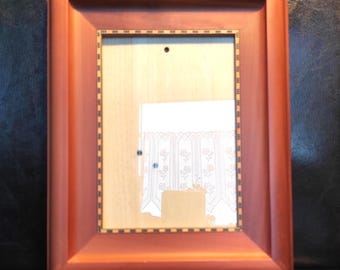 May include: A rectangular wooden picture frame with a smooth, reddish-brown finish. The inner border features a decorative inlay pattern of small, alternating black and white squares. The center is a light-colored, flat backing board.