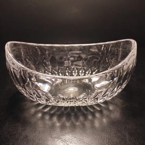 May include: A clear, oval-shaped glass bowl with a textured, cut-glass design. The bowl has a wide opening and a decorative pattern around the base. The bowl is likely used for serving or display.