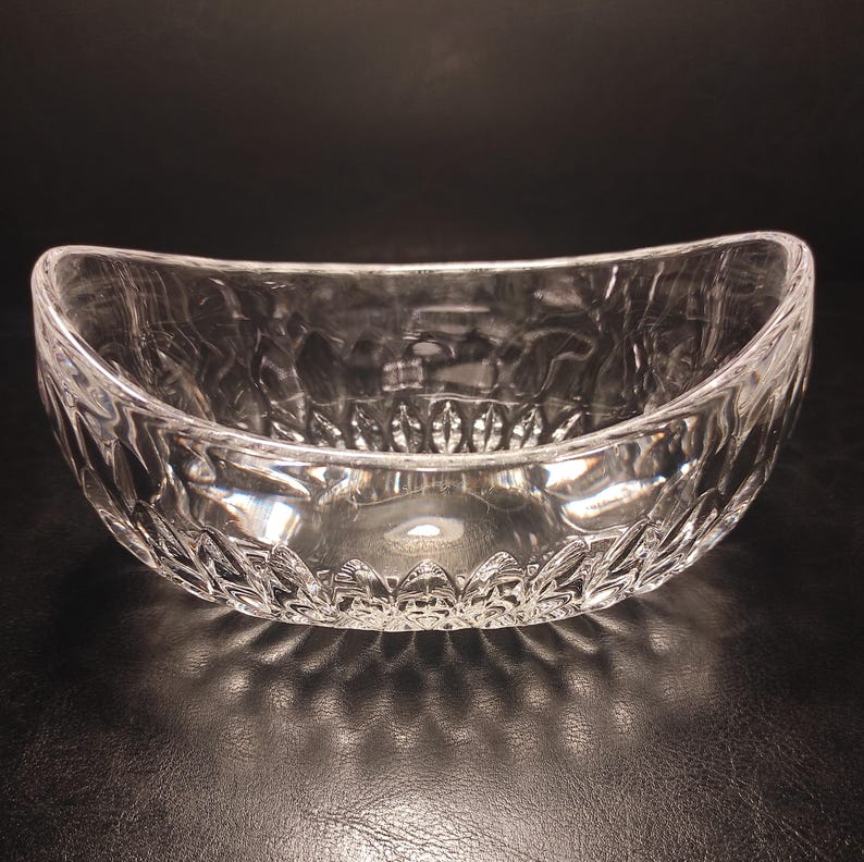 May include: A clear, oval-shaped glass bowl with a textured, cut-glass design. The bowl has a wide opening and a decorative pattern around the base. The bowl is likely used for serving or display.