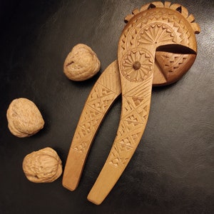 Op de afbeelding: Een houten notenkraker met ingewikkelde houtsnijwerk in de vorm van een vogel. De notenkraker is open en er liggen drie walnoten in de buurt.