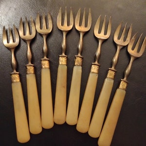 May include: Set of eight silver-tone forks with ivory-colored handles. The forks have three tines each and are arranged in a semi-circle.