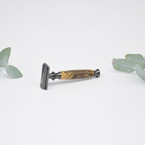 May include: A black safety razor with a bamboo handle. The razor has the word "BULL" engraved on the side.