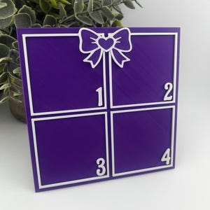 May include: A purple square divided into four sections, each numbered. A white bow-shaped design with a heart in the center is at the top. The numbers 1, 2, 3, and 4 are in white. The design is likely a decorative item.