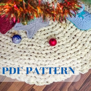 Könnte beinhalten: Weißer gestrickter Weihnachtsbaumrock mit einem roten und blauen Ornament oben. Der Text "PDF PATTERN" ist auf dem Rock gedruckt.