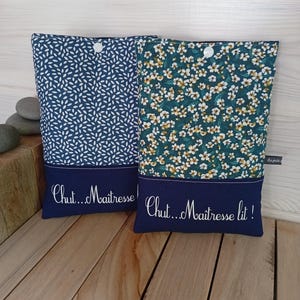 May include: Two fabric book sleeves with navy blue accents. One sleeve has a white leaf pattern on a navy background, the other has a floral pattern. Both have the text "Chut...Ma&icirc;tresse" and "Chut...Ma&icirc;tresse lit!" embroidered.