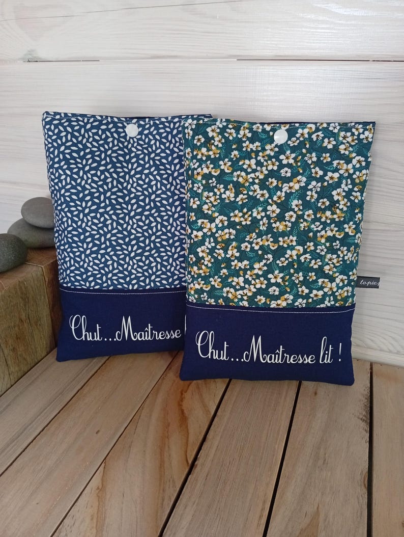May include: Two fabric book sleeves with navy blue accents. One sleeve has a white leaf pattern on a navy background, the other has a floral pattern. Both have the text "Chut...Ma&icirc;tresse" and "Chut...Ma&icirc;tresse lit!" embroidered.