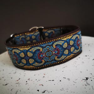 Op de afbeelding: Een bruin en blauw gepatroneerd hondenhalsband met een zilveren gesp. De halsband heeft een paisley-ontwerp met gouden accenten.