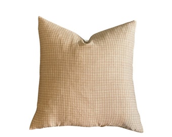May include: A beige square pillow with a subtle grid pattern. The pillow is made of a soft, textured fabric.