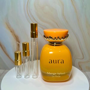 May include: Three small clear glass bottles with gold tops and a larger yellow glass bottle with a gold top and a gold label that says "aura Manga Splash La Fede".