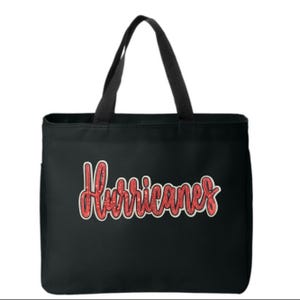 May include: Black tote bag featuring the word "Hurricanes" in red, glittery script. The bag has black handles and a side pocket. The text is outlined in white.