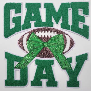 Puede incluir: Letras de fieltro verde aplicadas que deletrean "GAME DAY" con un balón de fútbol marrón y blanco con un lazo de lentejuelas verdes en el centro.