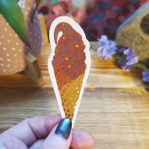 May include: A chocolate ice cream cone with colorful sprinkles. The cone is a waffle cone and the ice cream is in a swirl shape.
