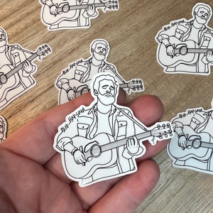 May include: A set of six black and white line art stickers featuring a man playing a guitar. The stickers have the text "Glen Hansard" on them.