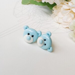 May include: A pair of blue teddy bear stud earrings. The teddy bears have white faces and black eyes.