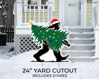 May include: A yard cutout featuring a black Bigfoot carrying a green Christmas tree decorated with colorful ornaments and a gold star. The Bigfoot wears a red Santa hat. The sign is 24 inches tall and includes stakes.