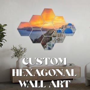 May include: Custom hexagonal wall art featuring a scenic landscape with a sunset over the ocean and white buildings with blue domes. The wall art is displayed on a white wall above a wooden cabinet. The text "CUSTOM HEXAGONAL WALL ART" is displayed below the wall art.