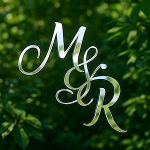 May include: A reflective silver monogram featuring the intertwined letters "M" and "R" in an elegant, cursive script. The letters are set against a blurred background of green foliage, creating a sophisticated and natural aesthetic.